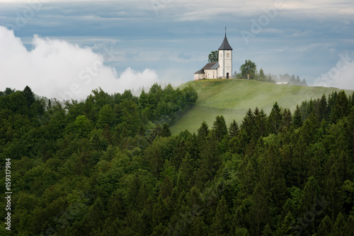 Jamnik church on a hillside in the spring, foggy weather at sunset in Slovenia, Europe. Mountain landscape shortly after spring rain. Slovenian Alps. 