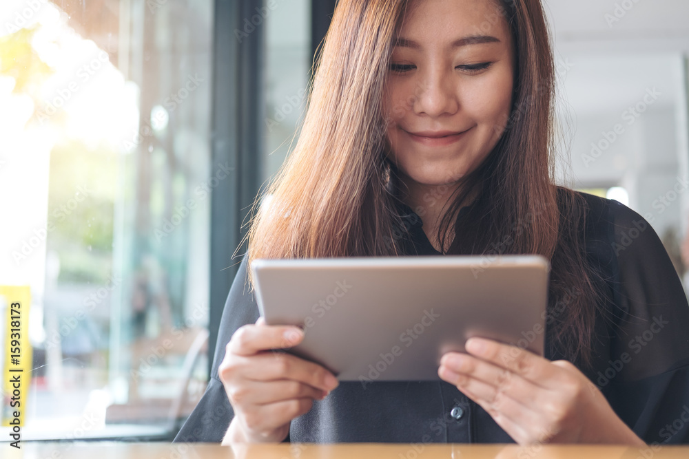 A beautiful Asian woman with smiley face holding and using tablet pc in modern cafe