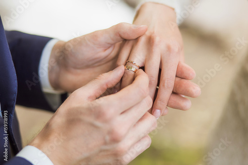 White bridal couple at wedding ceremony outdoors. Closeup of young happy beautiful bride and handsome groom holding hands and exchanging golden rings. Horizontal color picture.