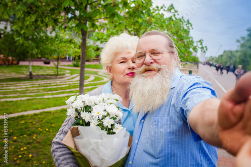 elderly couple walking around the park with a bouquet of flowers and make selfie