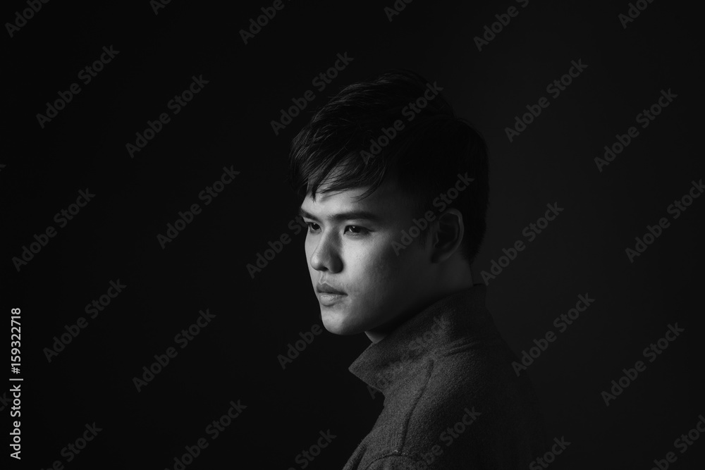 Attractive asian man looking down to his side on dark studio background.