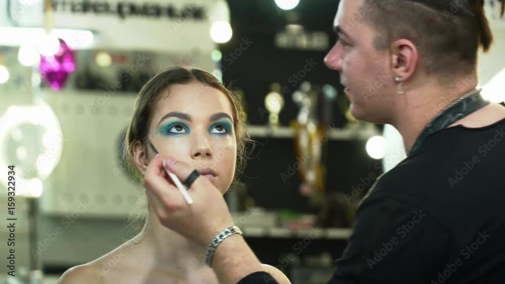 Makeup artist making the face art with blue shadows for a young woman in the studio closeup Makeup artist making the face art with blue shadows for a young woman in the studio closeup