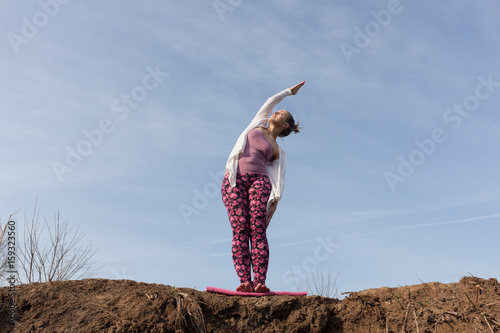 young woman performing yoga side stretch while standing on pile of soil