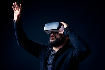 Young hipster bearded man wearing virtual reality goggles. Black background studio VR concept.