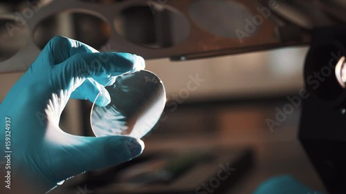 Engineer in blue rubber gloves cleaning lens with cotton swab at manufacture in bright bulb light