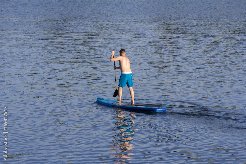Naklejka premium Man on Paddle Board paddling out to lake