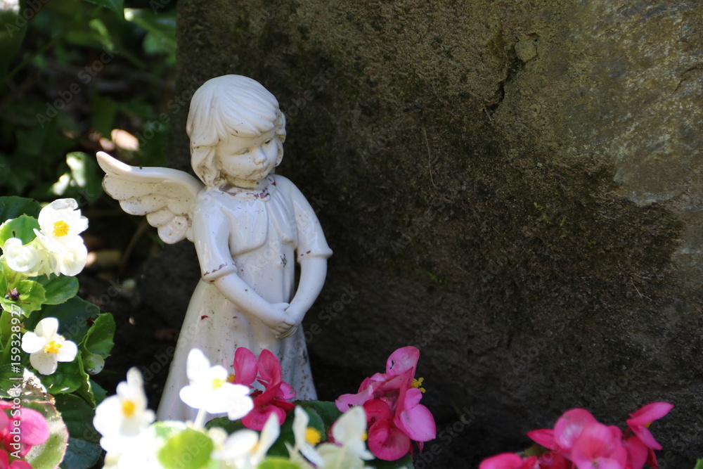 Engel auf dem Friedhof neben Blumen vor Grabstein