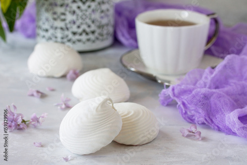 Delicate vanilla marshmallow on a white delicate plate. Still life with marshmallows, a cup of tea and lilac lilac on a background of ancient stone.