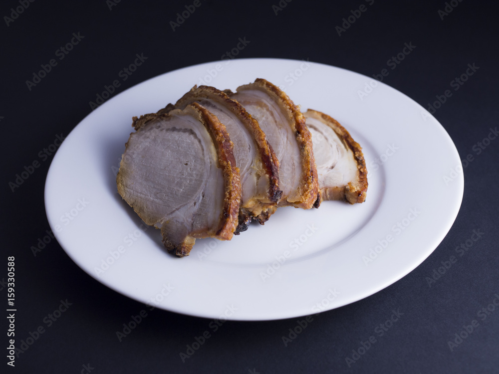 Slices of roasted pork with crispy crackling on white plate, isolated on black background Slices of roasted pork with crispy crackling on white plate, isolated on black background