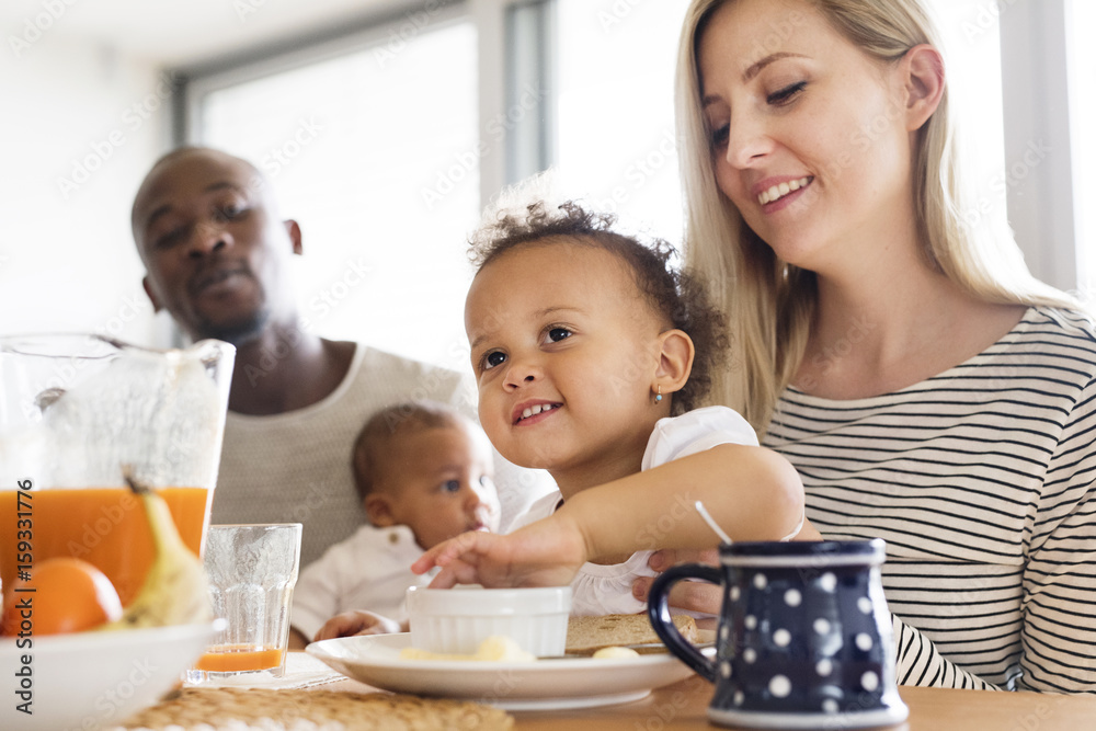 Young interracial family with little children having breakfast.