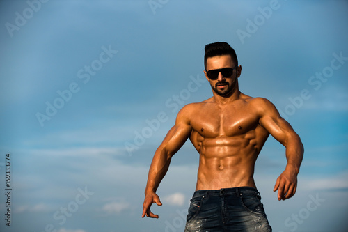sexy man with muscular body in sunglasses on blue sky