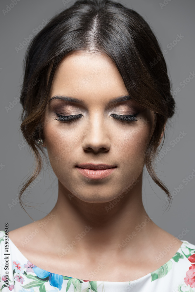 Fototapeta premium Close up vertical portrait of pretty young woman face with make up and perfect olive skin complexion over gray studio background.