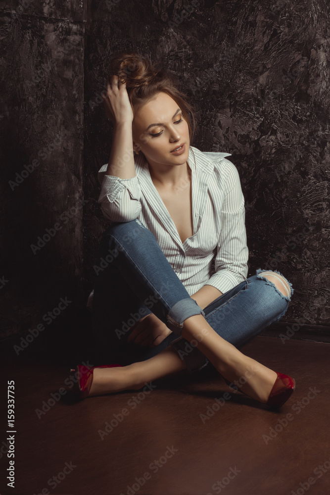 Wonderful young woman in shirt and jeans sitting on the floor