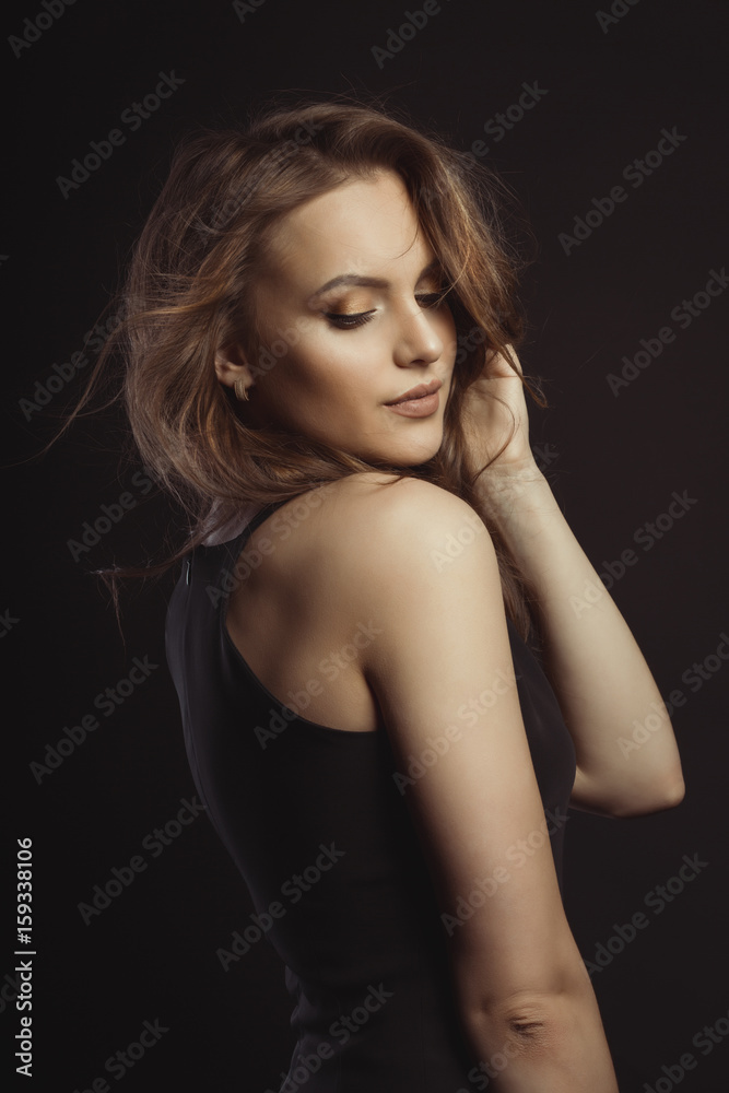 Glamorous brunette model in black dress with curly hair at studio