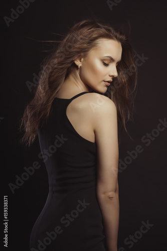 Stylish brunette model in black dress with curly hair in motion