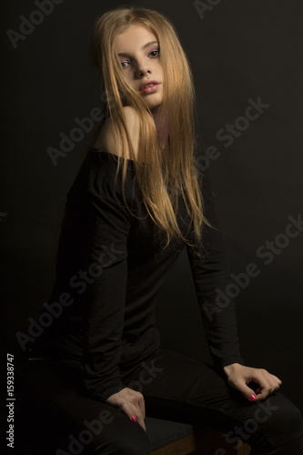 Stylish young woman with glitter on her neck posing at the dark room