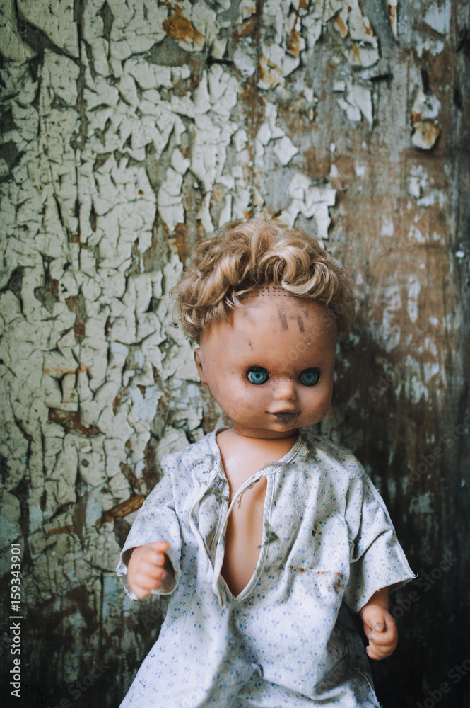 The old doll sits on the background of a wall with cracked paint. fear. horror.