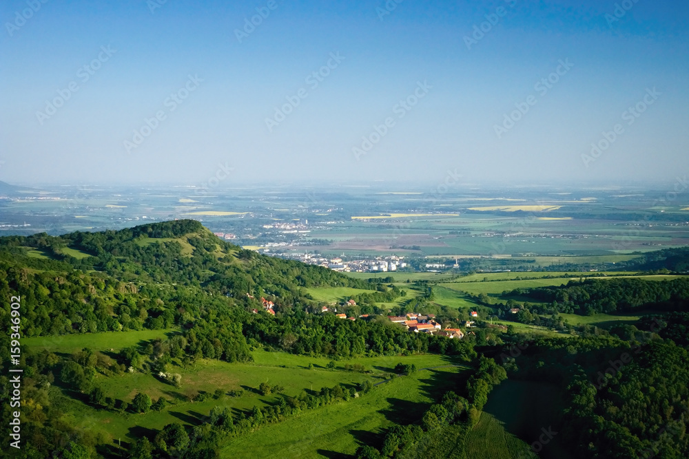 Ceske Stredohori tourist area with hill Kamyk and Litomerice city on horizont and Kundratice village in foreground in spring evening czech landscape during sunset