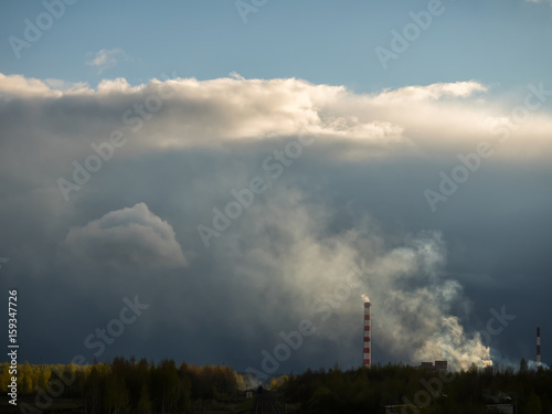 Dense clouds of smoke or a pair of two pipes against a cloud background. The railway with a train going into the distance. The concept of ecology, pollution of the environment