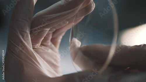Hands in white rubber gloves cleaning round glass lens against white light using cloth piece in laboratory, close up