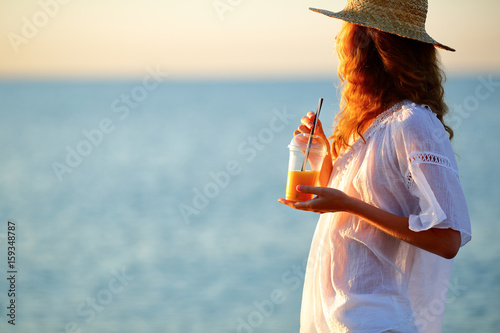 Young woman with orange juice in disposable cup against the sea