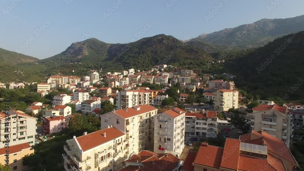 Drone flight above modern hotel houses red roofs Budva Montenegro surrounded by great mountains. Tile roofs. Summer sunny day Drone flight above modern hotel houses red roofs Budva Montenegro surrounded by great mountains. Tile roofs. Summer sunny day