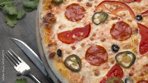 Large pizza with tomatoes and hot peppers next to the fork and knife on the table photo