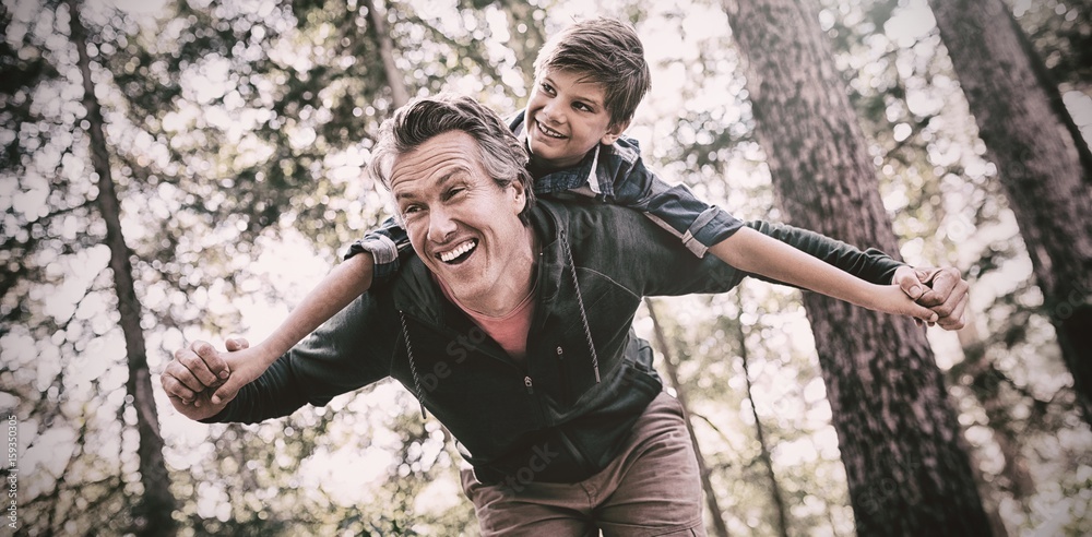 Cheerful father piggybacking son in forest