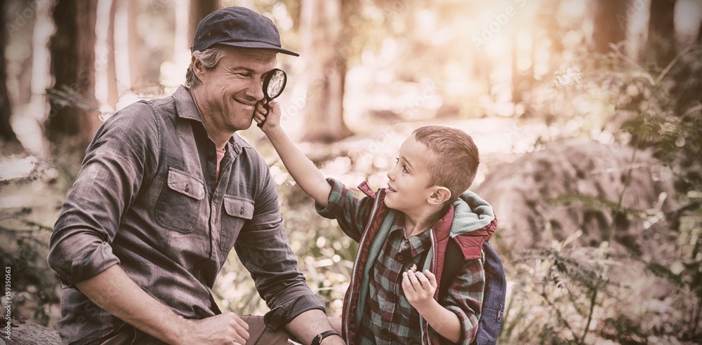 Boy showing magnifying glass to father while hiking in forest