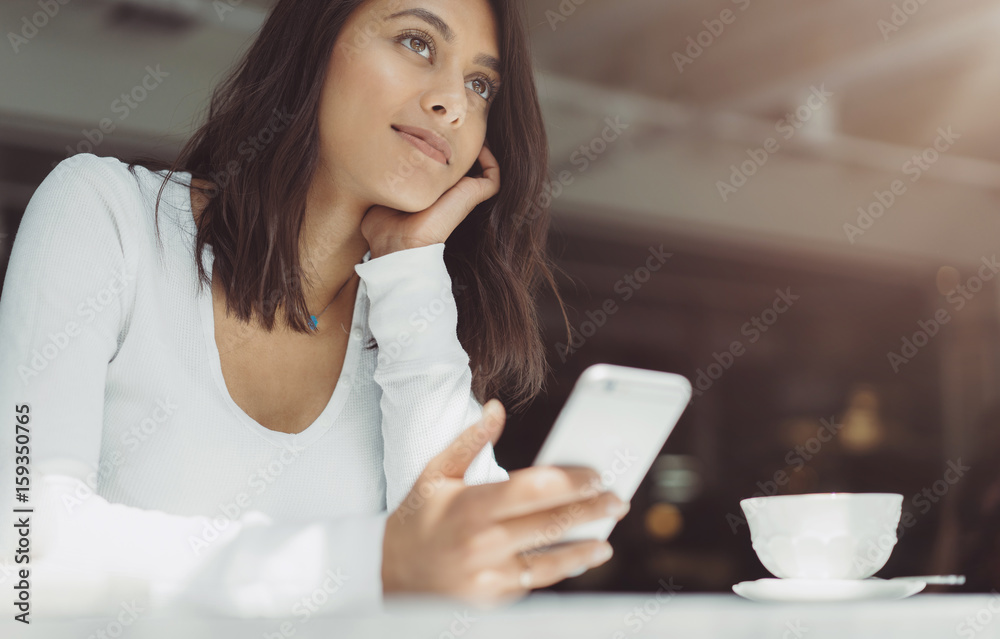 Portrait beautiful young woman with cup of coffee sitting at cafe and looking away, Charming smiling hipster girl received good news on cell telephone while she sitting in cozy coffee shop Portrait beautiful young woman with cup of coffee sitting at cafe and looking away, Charming smiling hipster girl received good news on cell telephone while she sitting in cozy coffee shop