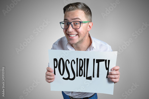 Funny laughing guy (men, student, businessman) of european appearance in casual clothes and glasses is holding a white sheet with text Possibility!