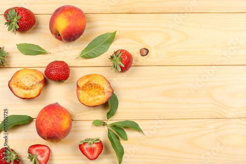 peach fruit with strawberry and green leaf on light wooden background. top view with copy space