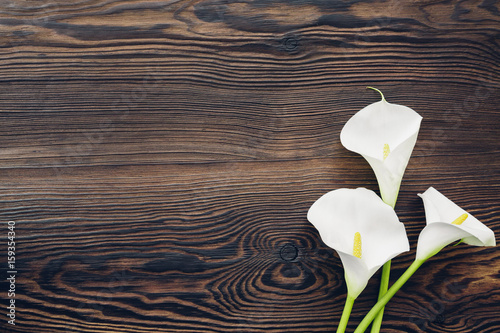 Fotografija White calla flowers on wooden background, top view