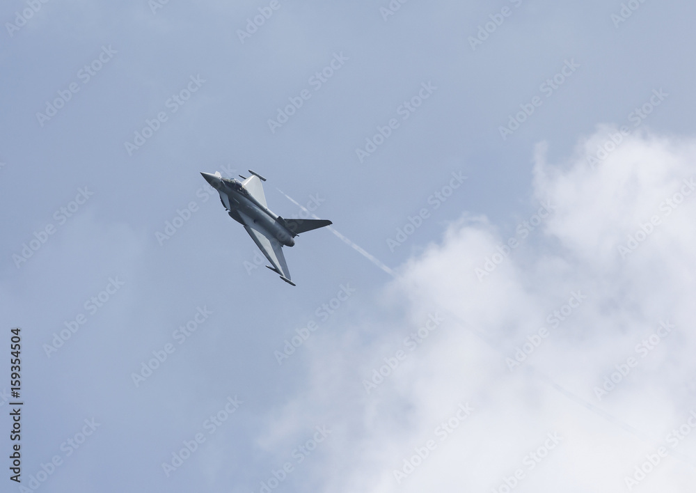 Obraz premium Modern jet fighter flying high against the gray sky with some clouds.