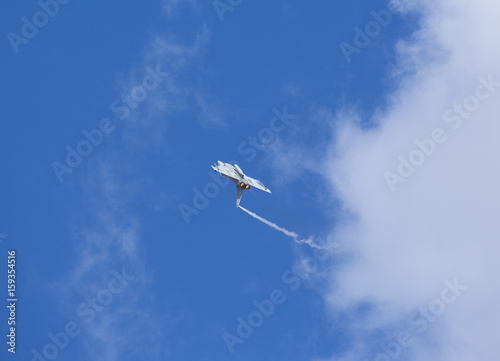 Modern jet fighter flying high against the blue sky with some clouds. Afterburner glowing orange.