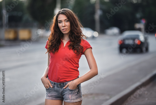 Summer outdoor porttrait of young pretty girl posing at sunset in city