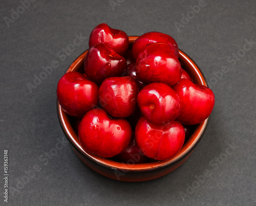 Pile of red glossy sweet cherries in brown earthenware saucer
