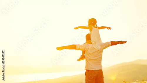 father's day. child daughter sits on her dad shoulders outdoors on a summer