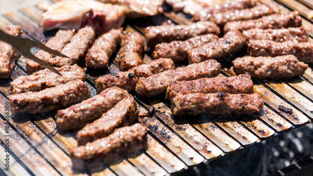 Grilling minced meat on a barbecue grill with coal; outdoors picnic with minced pork meat rolls (also known as mici, mititei, cevapi or cevapcici) Grilling minced meat on a barbecue grill with coal; outdoors picnic with minced pork meat rolls (also known as mici, mititei, cevapi or cevapcici)