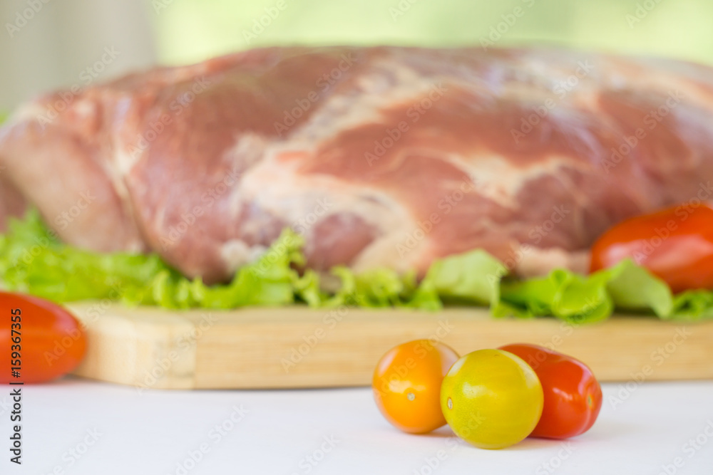 Raw cervical carbonate of pork on cutting board with leaves of green salad, vegetables, tomatoes, parsley and onion, isolated on white background Raw cervical carbonate of pork on cutting board with leaves of green salad, vegetables, tomatoes, parsley and onion, isolated on white background