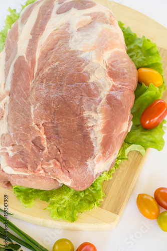 Raw cervical carbonate of pork on cutting board with leaves of green salad, vegetables, tomatoes, parsley and onion, isolated on white background