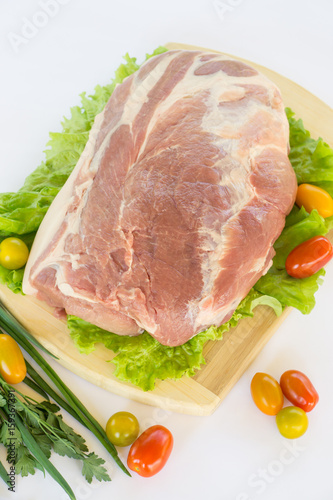 Raw cervical carbonate of pork on cutting board with leaves of green salad, vegetables, tomatoes, parsley and onion, isolated on white background