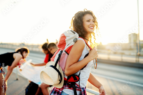 Beautiful young woman with red backpack exploring city with her friends. Portrait of beautiful female tourist at street.
