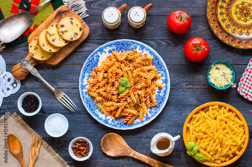 Fusilli pasta with tomato sauce, tomatoes, onion, garlic, dried paprika, olives, pepper and olive oil, on a wooden background.
