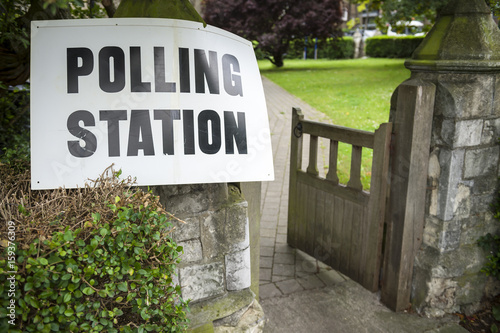 British election polling station sign hanging on post next to an open gate and hedge in the UK photo