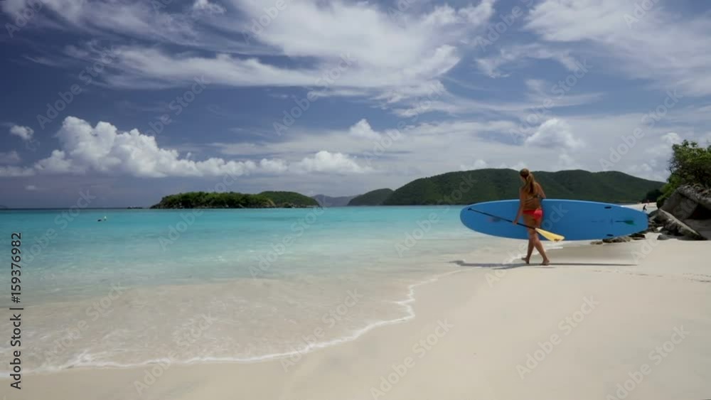 woman walking with paddle board on tropical beach, Cinnamon bay, st john woman walking with paddle board on tropical beach, Cinnamon bay, st john