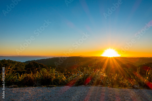 Beautiful sunset over the Hauraki Gulf, with trees and hills silhouetted in the foreground. Taken on the beach at Whakanewha Camp Ground on Waiheke Island, New Zealand photo