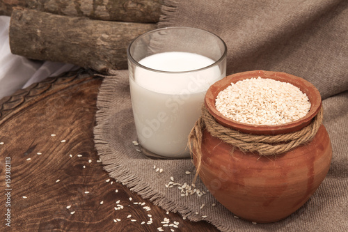 Sesame milk in glass and sesame seed in clay pot on a wooden table.