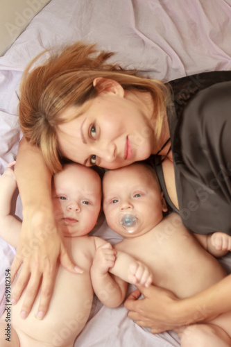 indoor portrait of young happy smiling mother with her twin babies at home