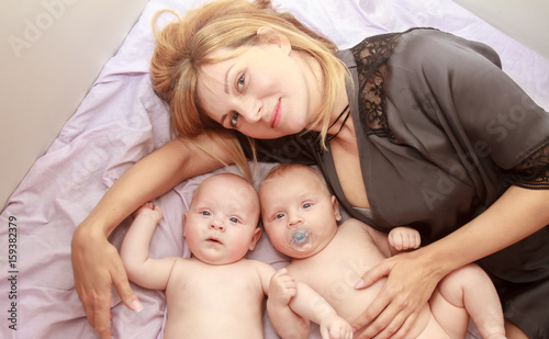 indoor portrait of young happy smiling mother with her twin babies at home